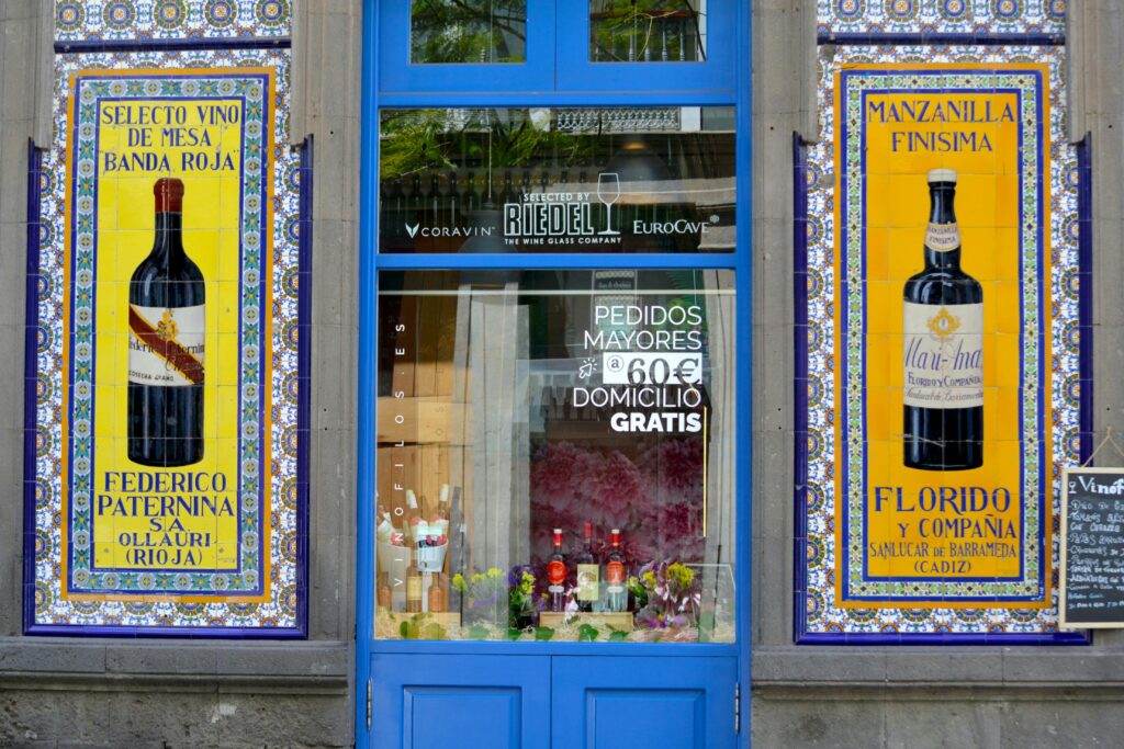 Vibrant shopfront in Cadiz with decorative wine posters and blue entrance.